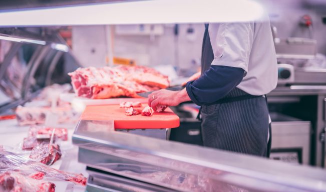 Un boucher prépare de la viande sur une planche à découper dans une boucherie.