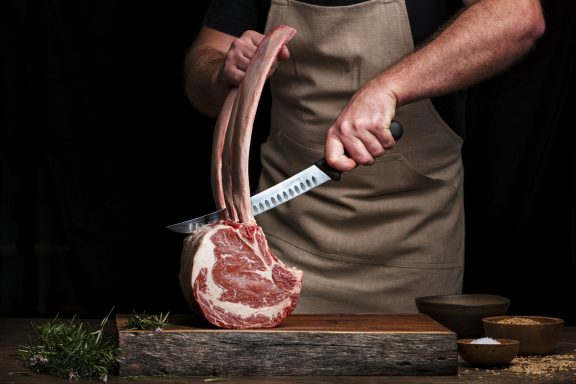 Un boucher découpe une côte de boeuf sur une planche en bois.