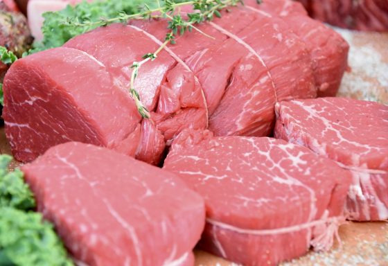 Viande rouge crue, avec des herbes et des morceaux de viande sur une planche en bois.